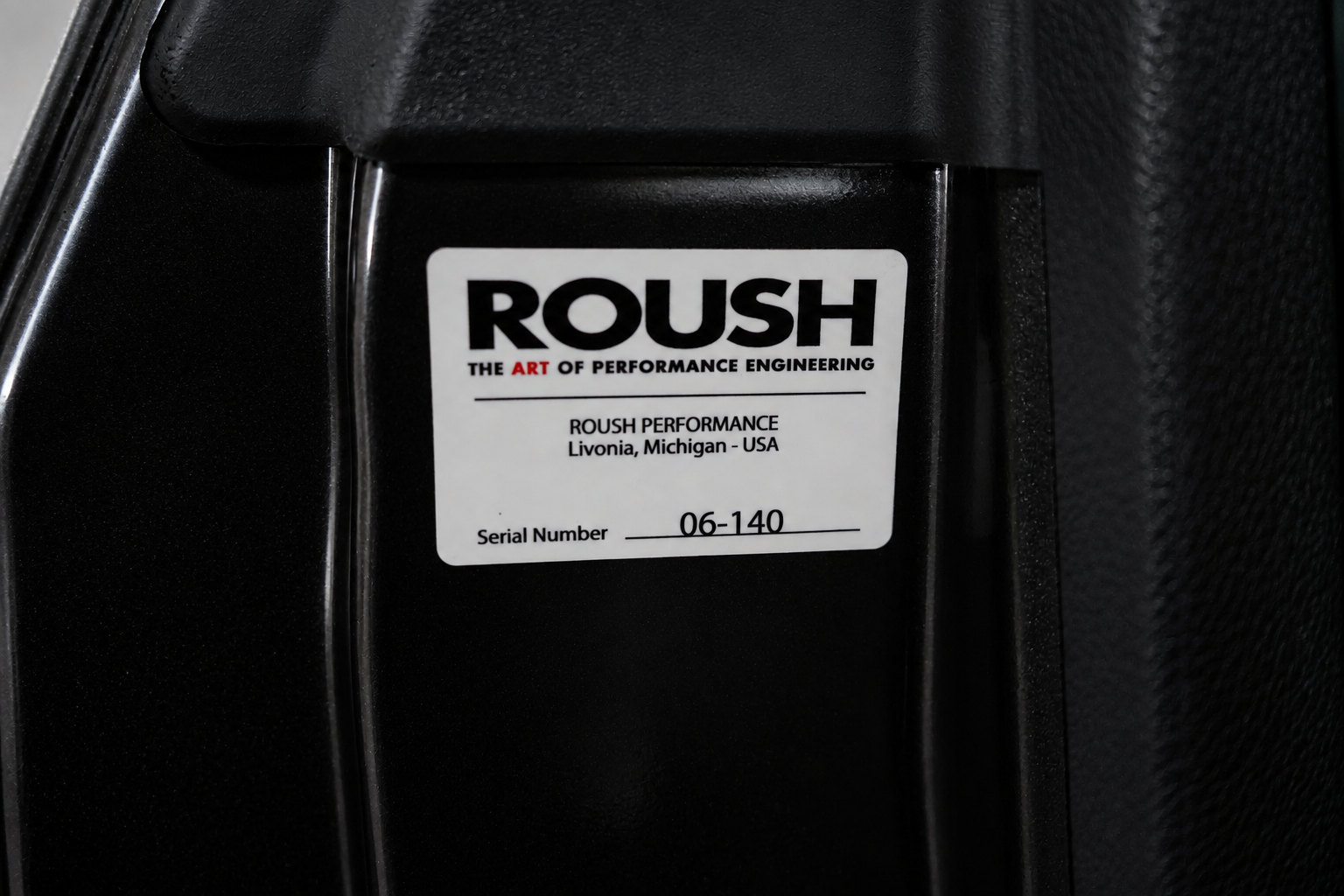 White ROUSH serial-number sticker reading “Serial Number 06-140” on a black vehicle panel, printed with the ROUSH wordmark and the words ROUSH Performance, Livonia, Michigan - USA.