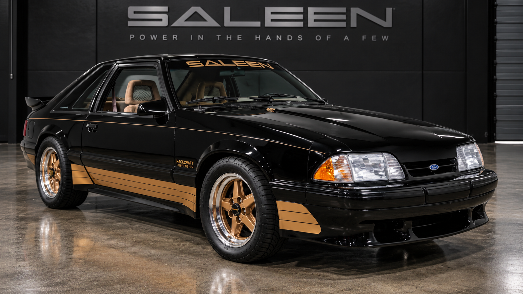 Black Fox-body Saleen Mustang with gold graphics and wheels, viewed from the front three-quarter angle.